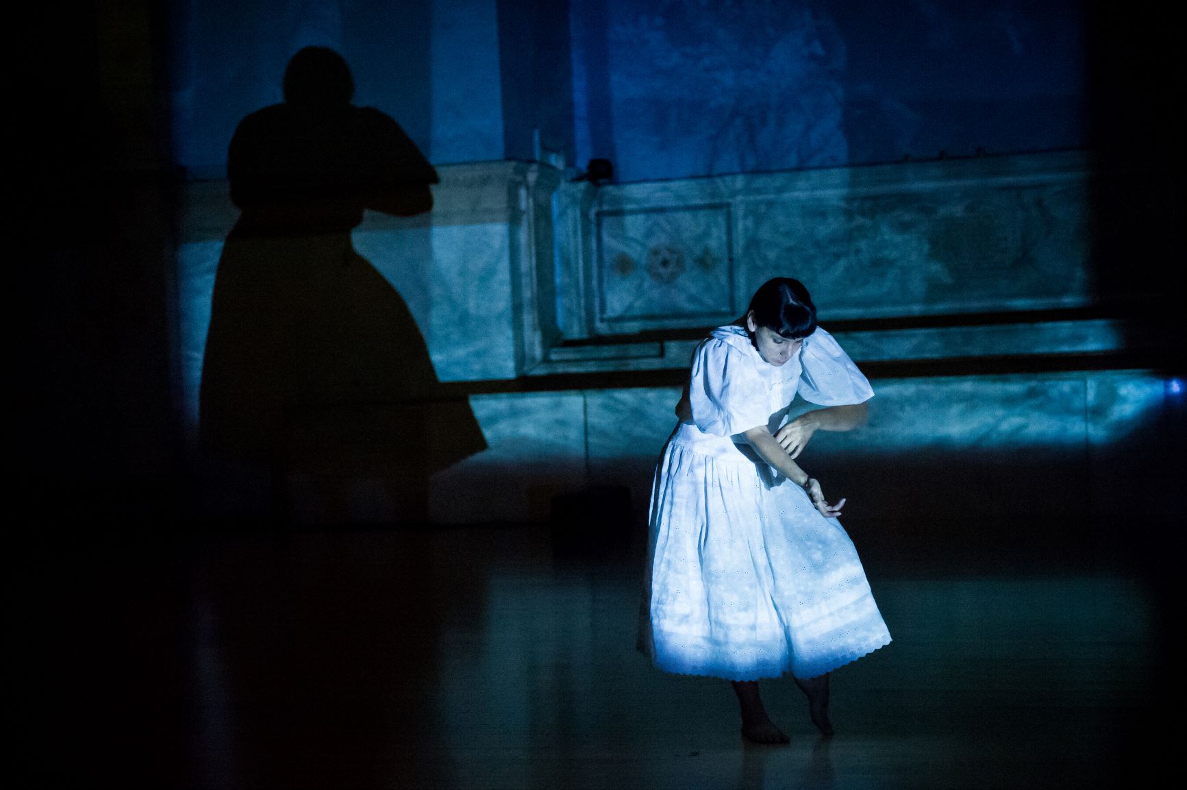 Simas, woman with dark hair, wearing a white dress leans over in forward bending motion